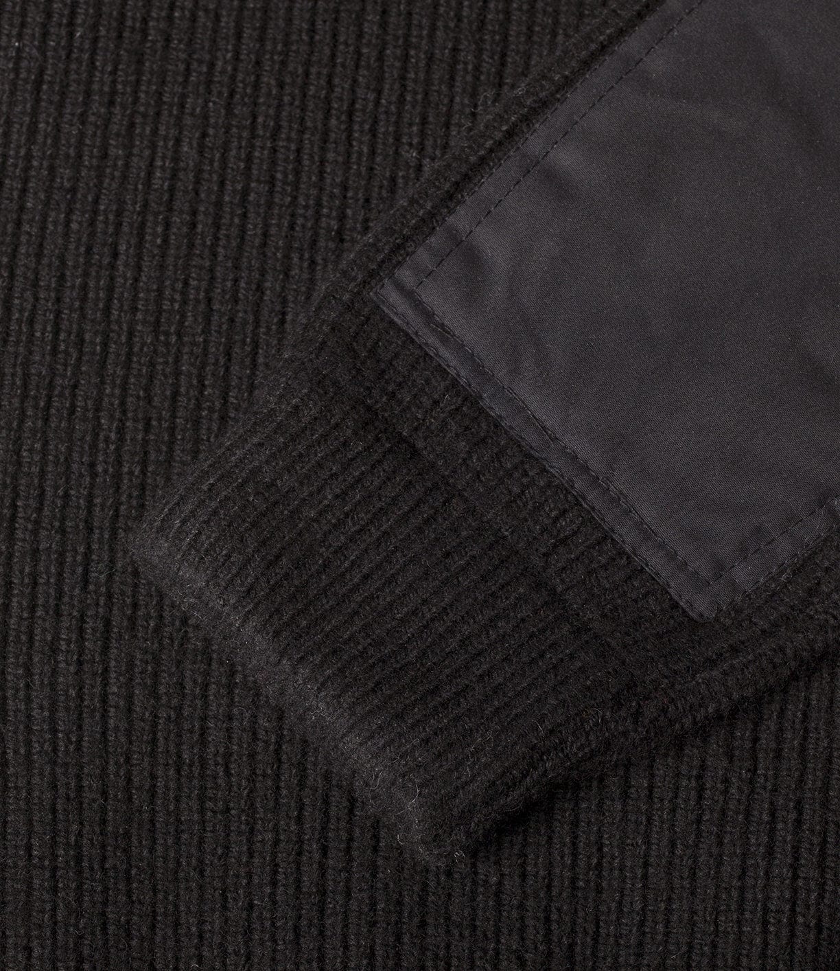 Close-up of a black ribbed fabric sleeve with a black rectangular patch sewn onto it.