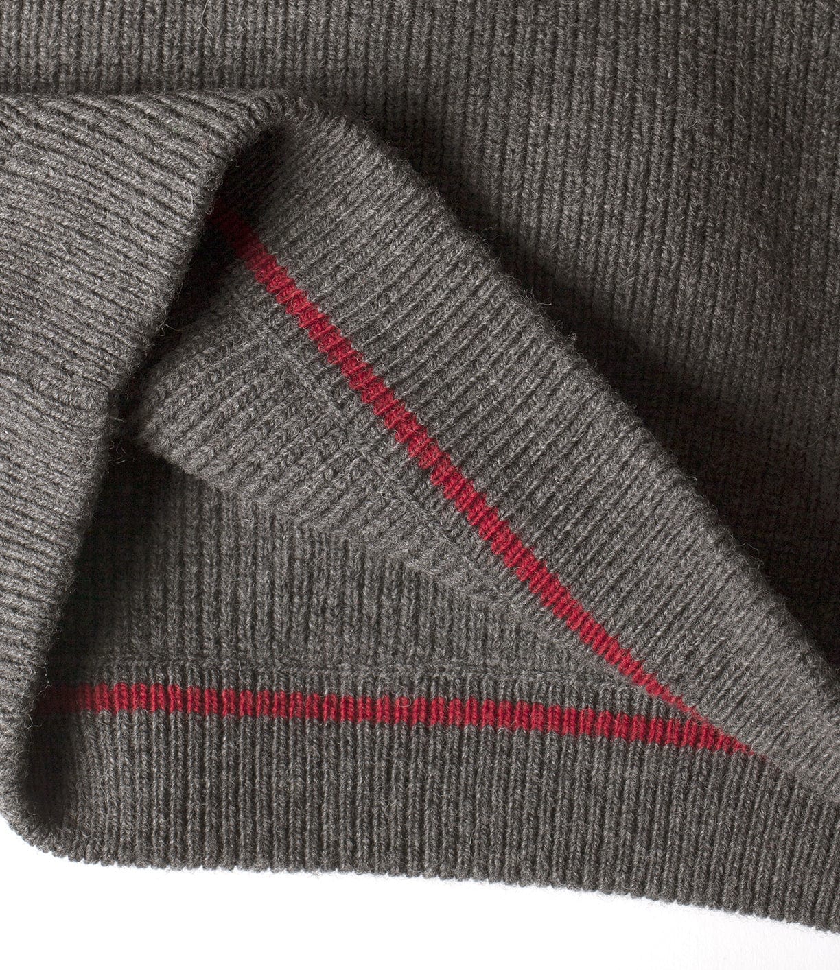 Close-up of a gray knitted fabric with a folded corner, featuring two parallel red stripes.