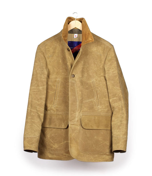 A tan waxed cotton jacket with a suede collar, hanging on a wooden hanger. It features two large front pockets, a button-front closure, and visible wear marks.