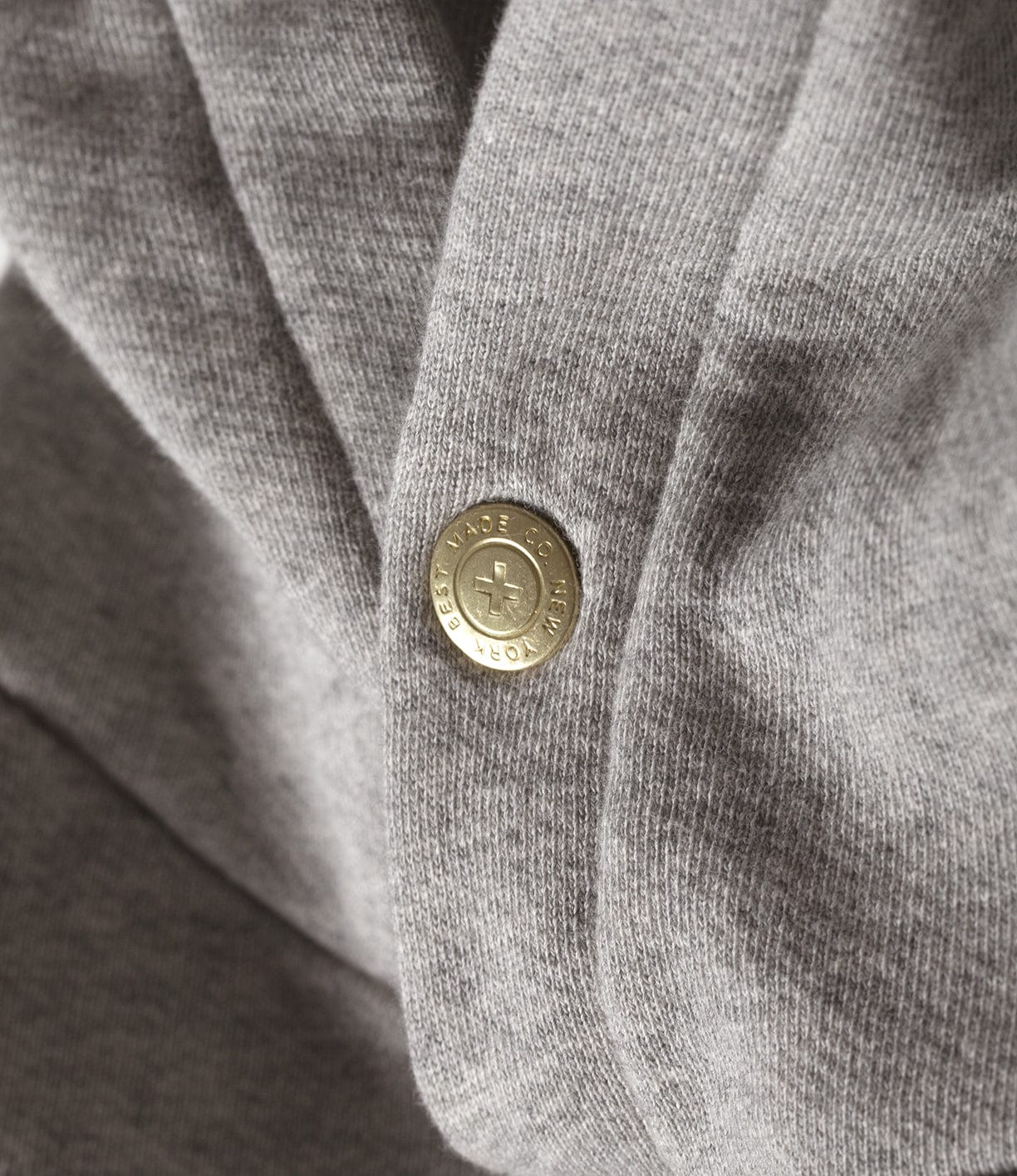 Close-up of a grey fabric with a metal snap button that has the text Eloise Jame and Crew.