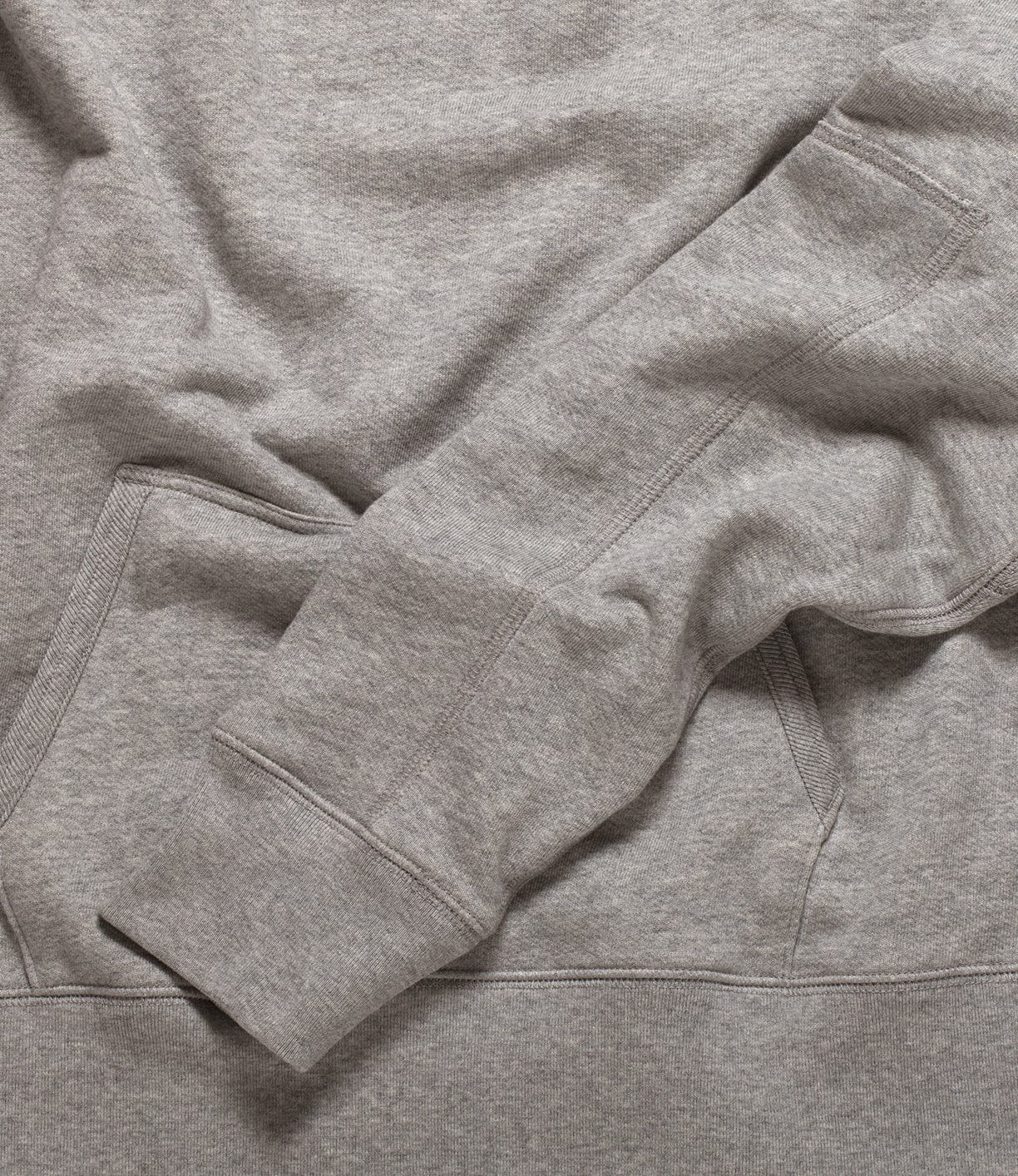 Close-up of a heather gray sweatshirt showing a sleeve and a kangaroo pocket. The fabric texture and stitching details are visible.