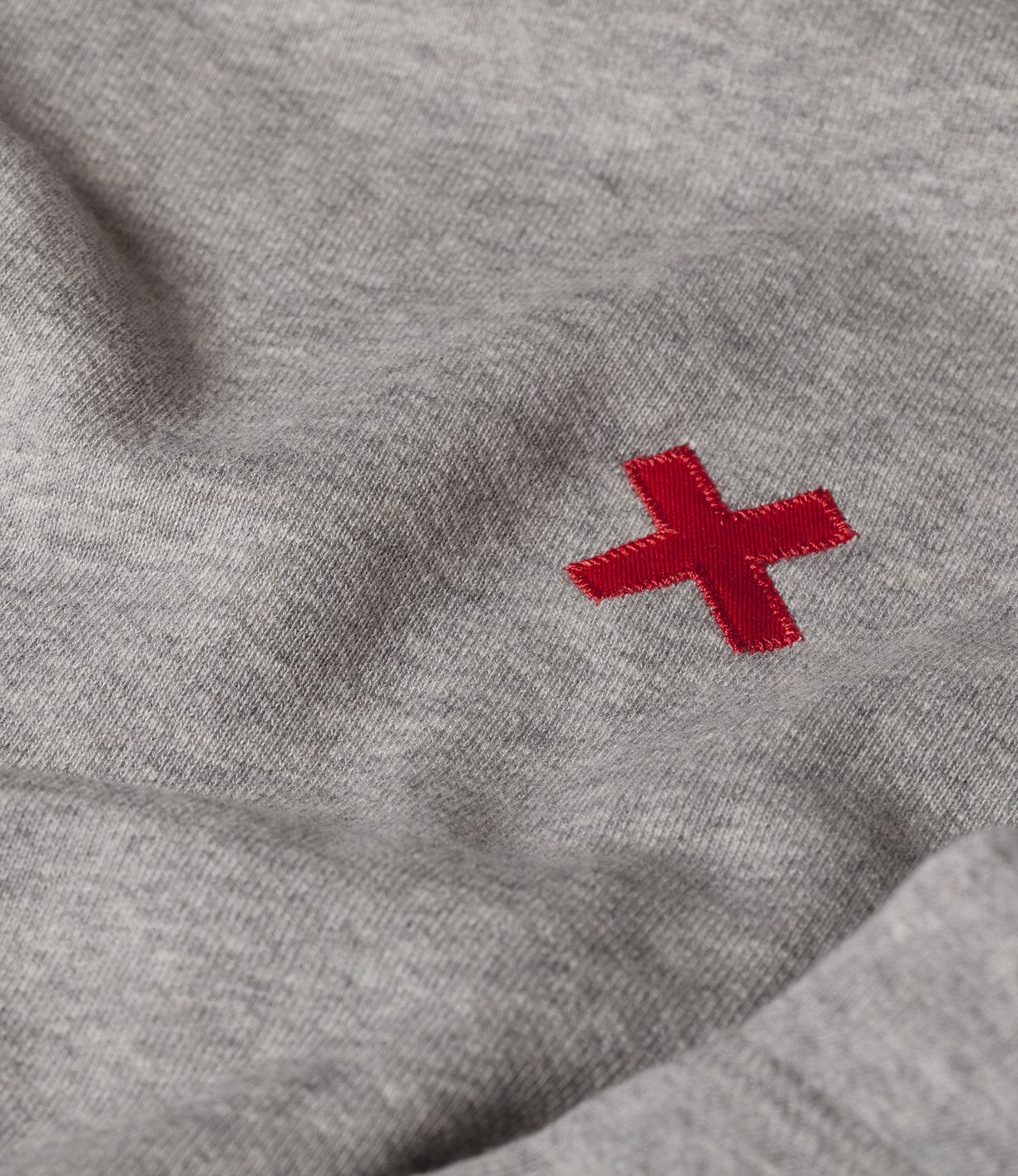 Close-up of a grey fabric with a small embroidered red cross symbol.