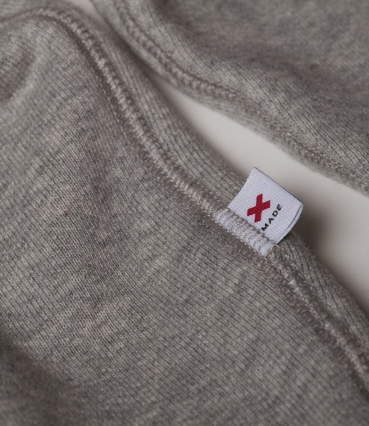 Close-up of a grey fabric garment with a visible seam and a small white tag featuring a red X.