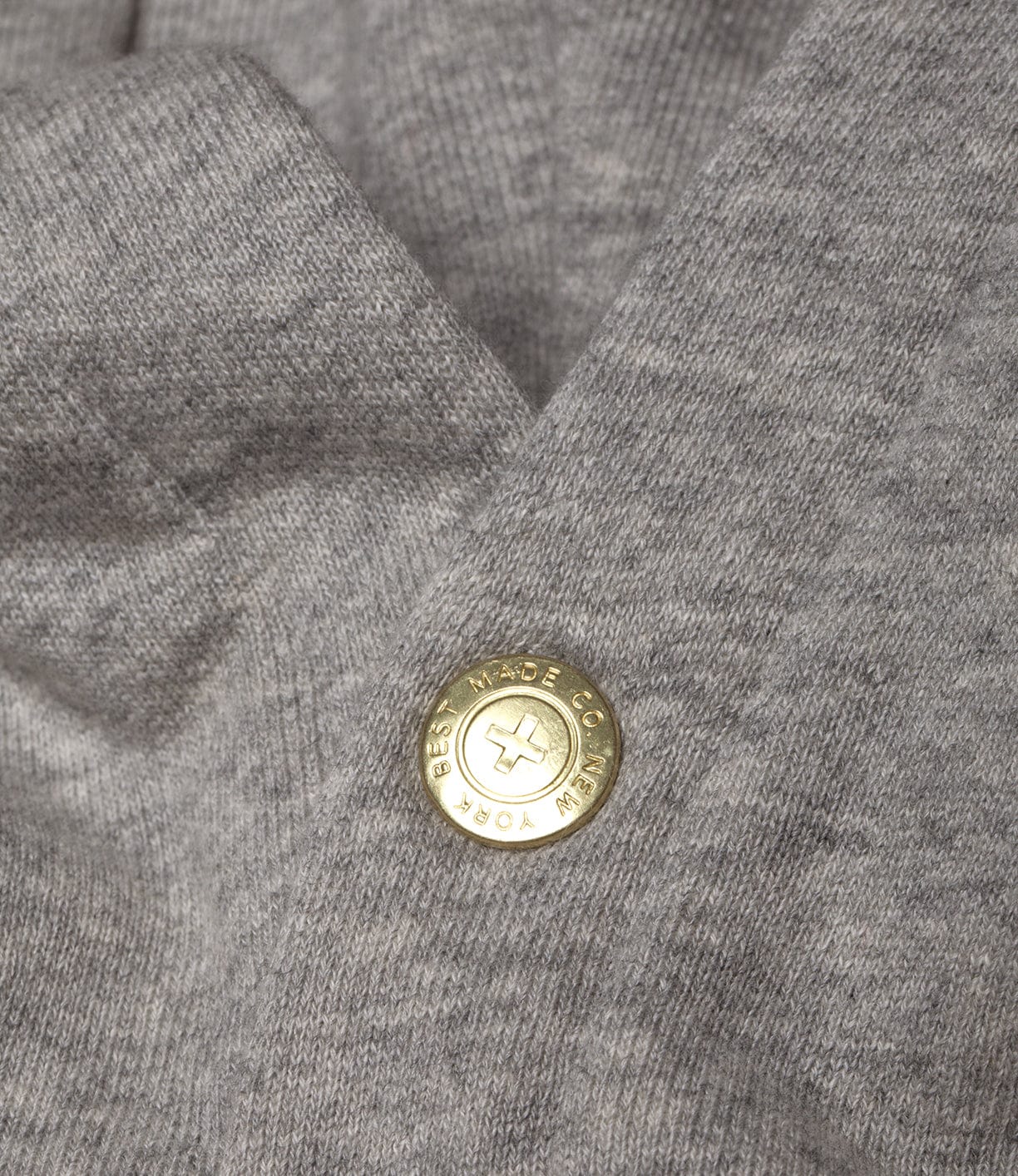 Close-up of a gray fabric with a round, gold-colored button displaying the text BEST MADE CO NEW YORK around the edge.