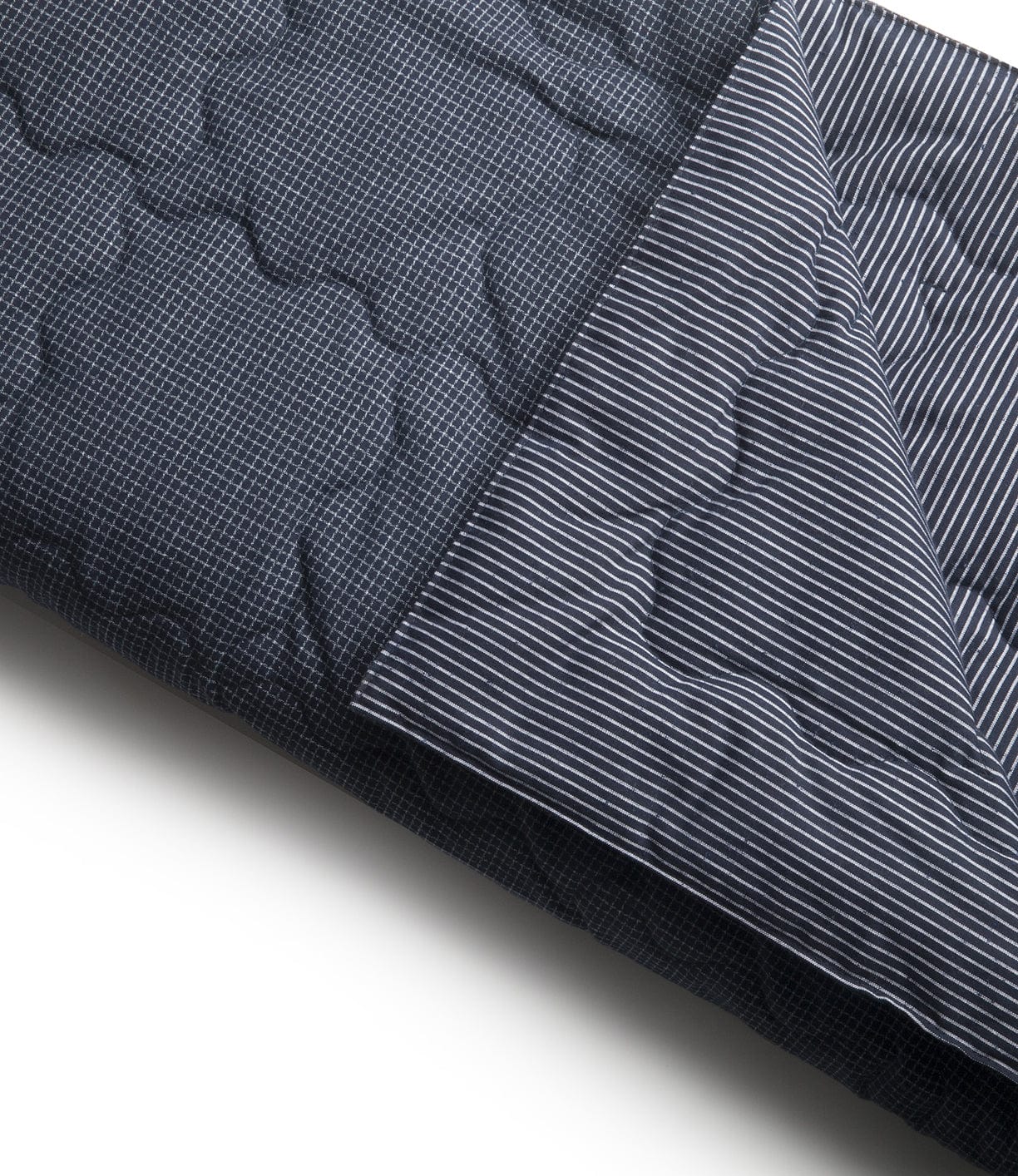 A dark blue quilt with a small checkered pattern on one side is shown partially folded to reveal a striped pattern on the other side.