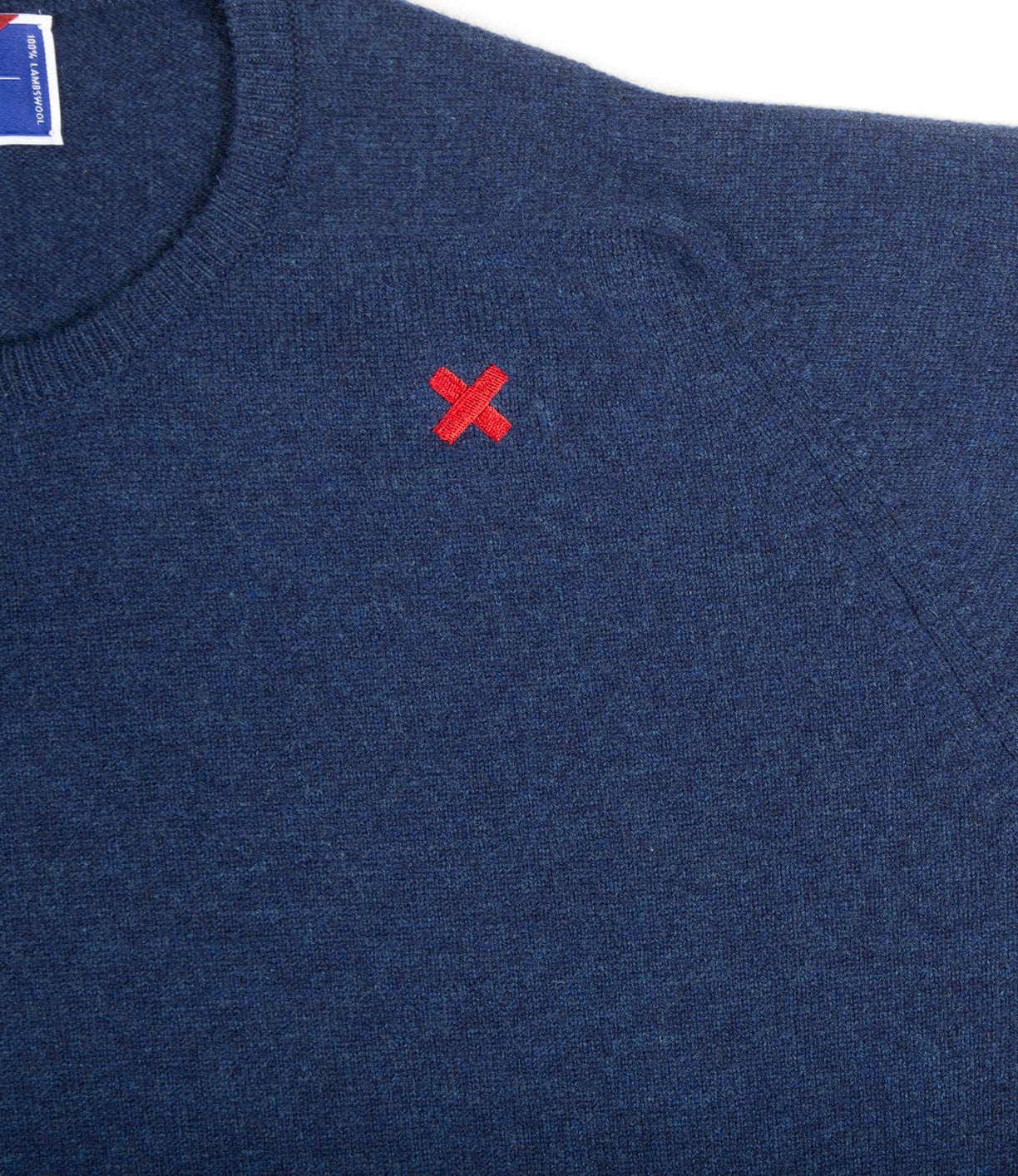 A close-up of a dark blue sweater with a small red X embroidered on the left chest area.