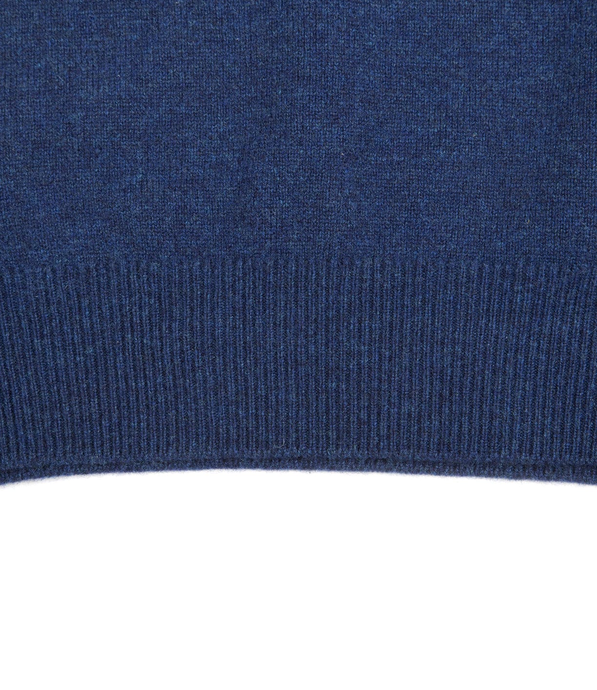 Close-up view of the bottom hem of a blue knitted fabric, displaying a ribbed texture.