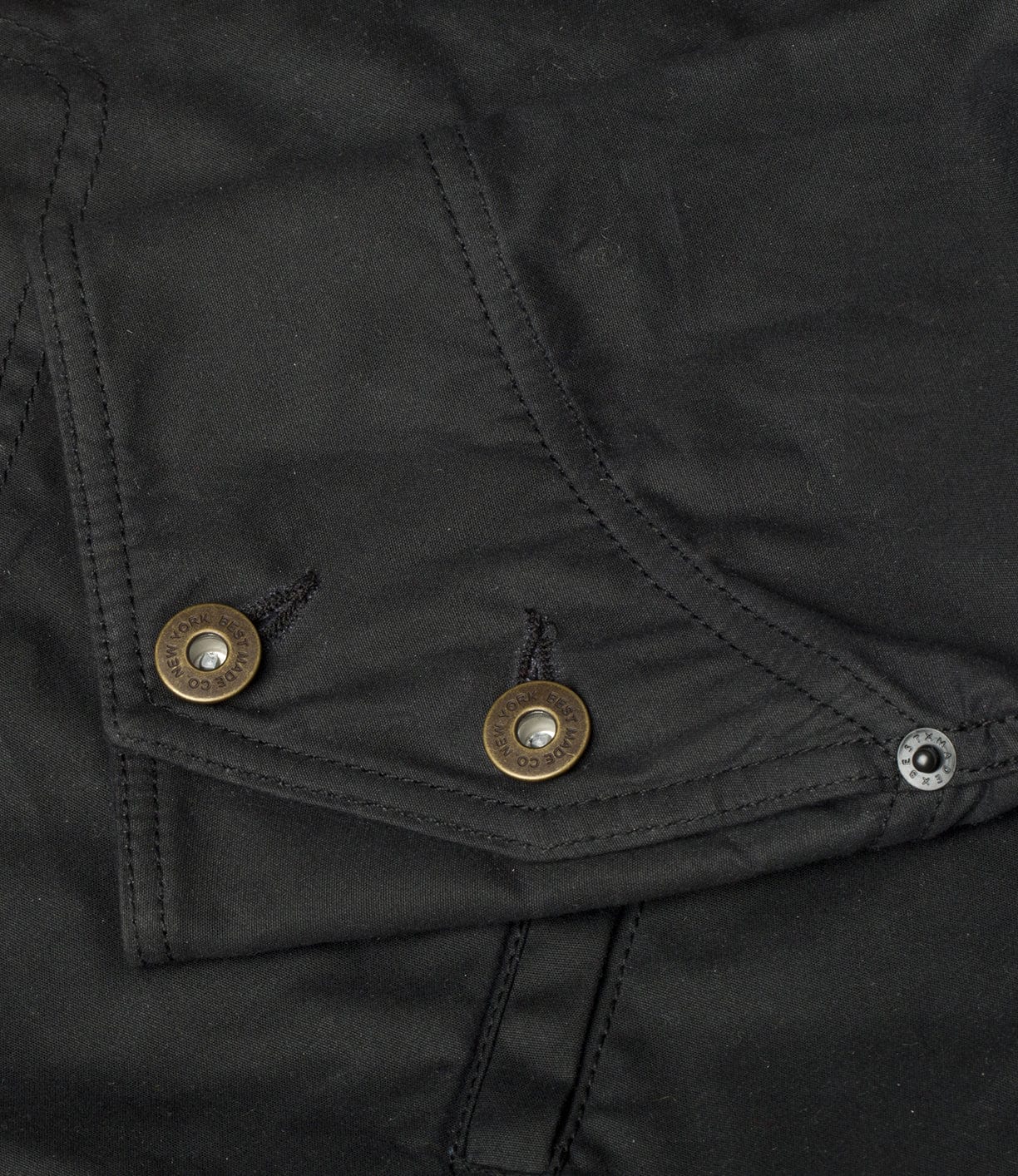 Close-up of a black fabric with two metal buttons and stitched pockets.