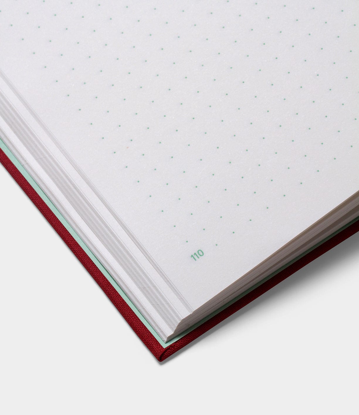 Close-up of an open notebook with dotted grid pages and a red cover. The page number 110 is visible.