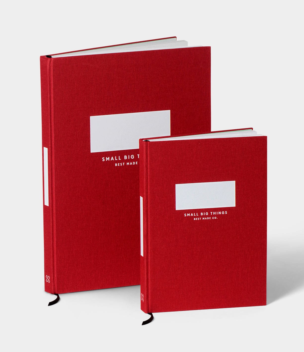 Two red hardcover books are standing side by side. The larger book has a label with SMALL BIG THINGS and BEST MADE text, while the smaller book has a label with SMALL BIG THINGS and BEST MADE CO text.