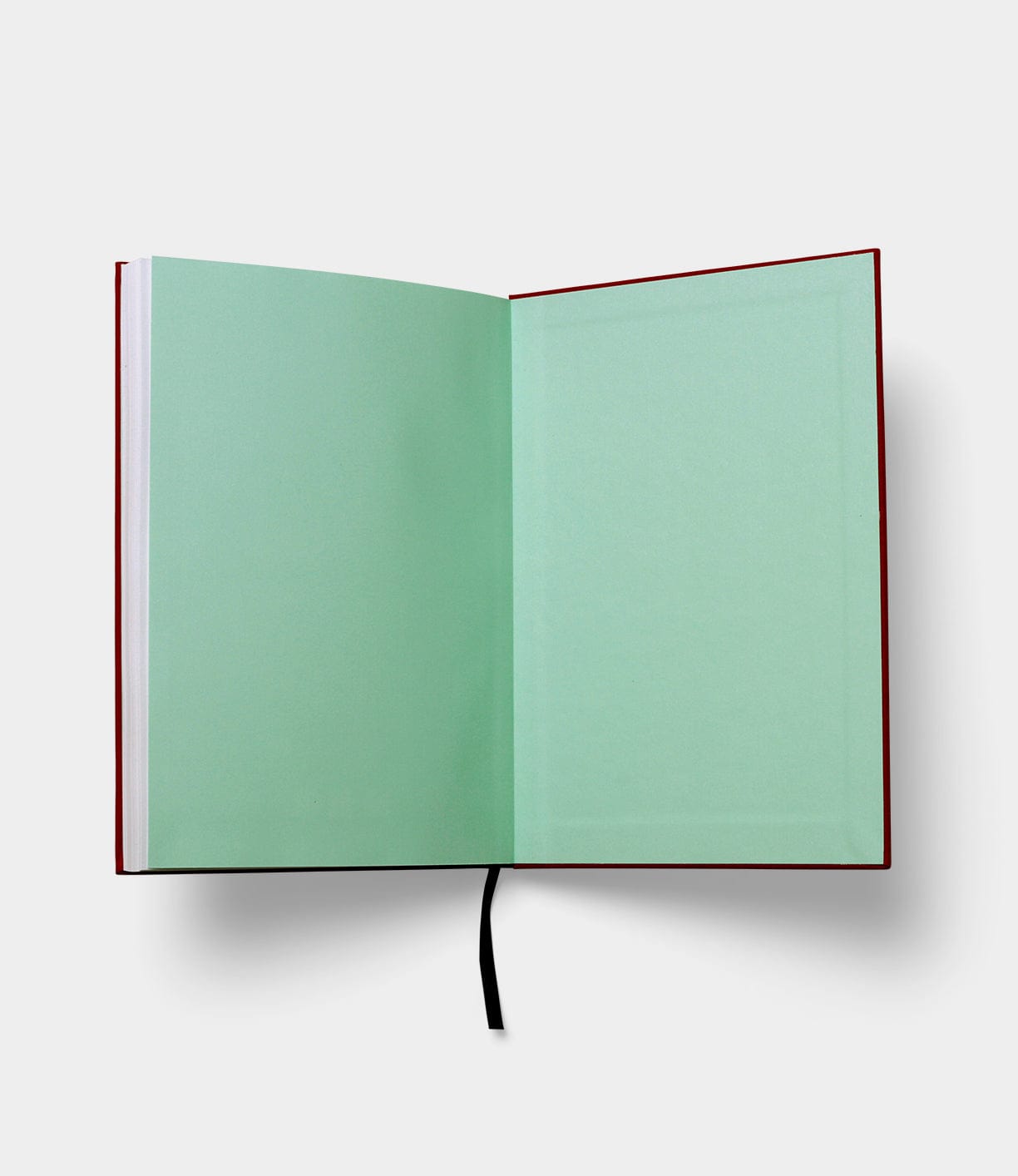 A red-bound book is open to a blank green page with a black ribbon bookmark lying in the middle.