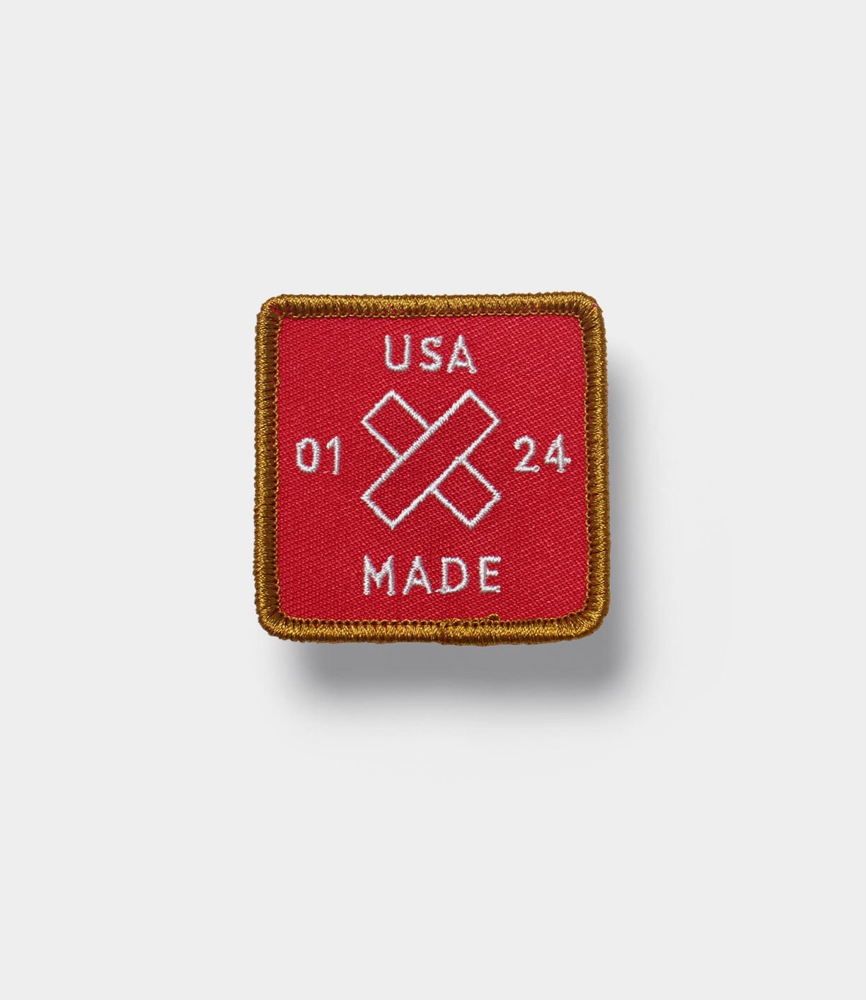 A square patch with a red background and gold border, displaying USA MADE with a cross and the numbers 01 24 in white.