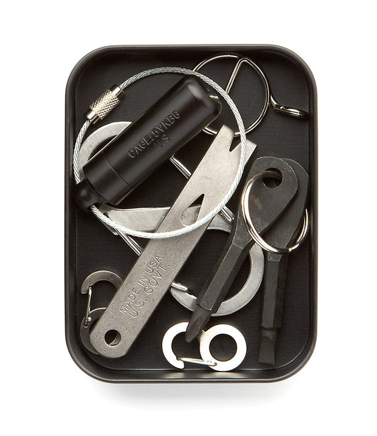 A compact survival kit including a cable saw, multipurpose tool, small blade, and other essential tools, stored in a rectangular black tin.