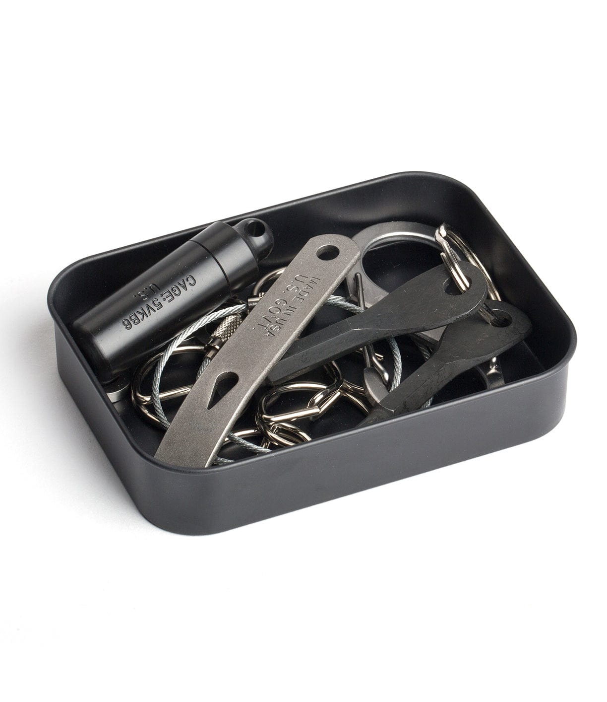 A black rectangular tray containing a small black cylinder canister and various metal tools and keychains.