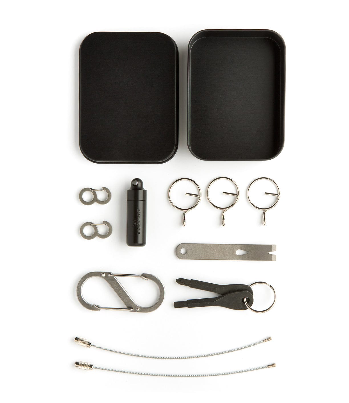 A flat lay image showing two open metal boxes, fishhooks, a small black capsule, rings, a pry bar tool, a carabiner, a keychain with tools, and metal wires arranged neatly on a white background.