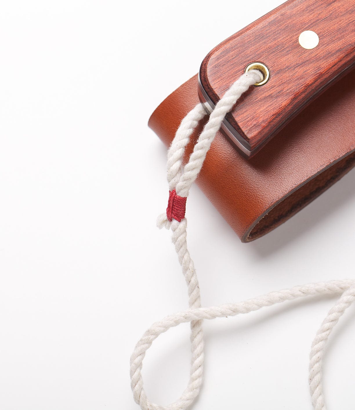 A close-up of a piece of brown leather and wood with a white rope threaded through a hole and secured with a red thread.