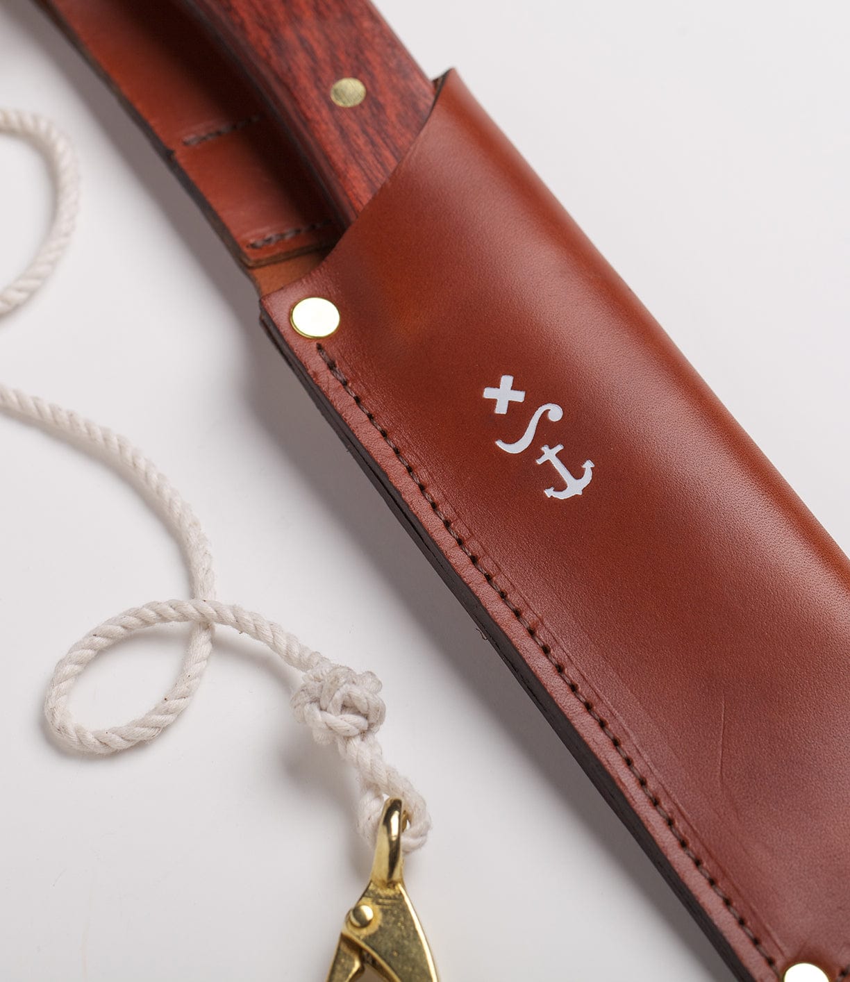 A knife with a wooden handle partially visible in a brown leather sheath next to a white rope with a brass clasp.