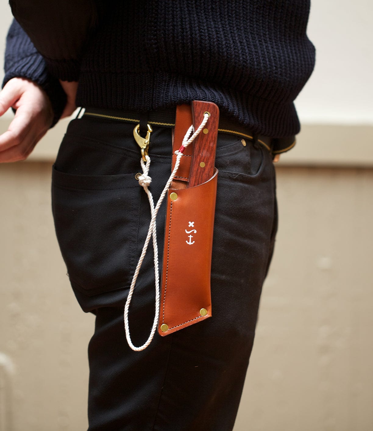 Person wearing a black sweater and pants, with a leather sheath holding a knife attached to their belt, secured with a white rope.