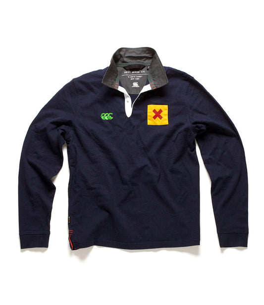 Navy blue rugby shirt with a contrasting black collar. It features a green logo on the left chest, a yellow and red patch on the right chest, and white buttons on the placket.