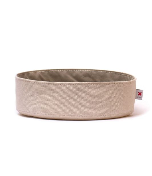 A round, beige fabric storage basket with a small white tag featuring a red X on the side.