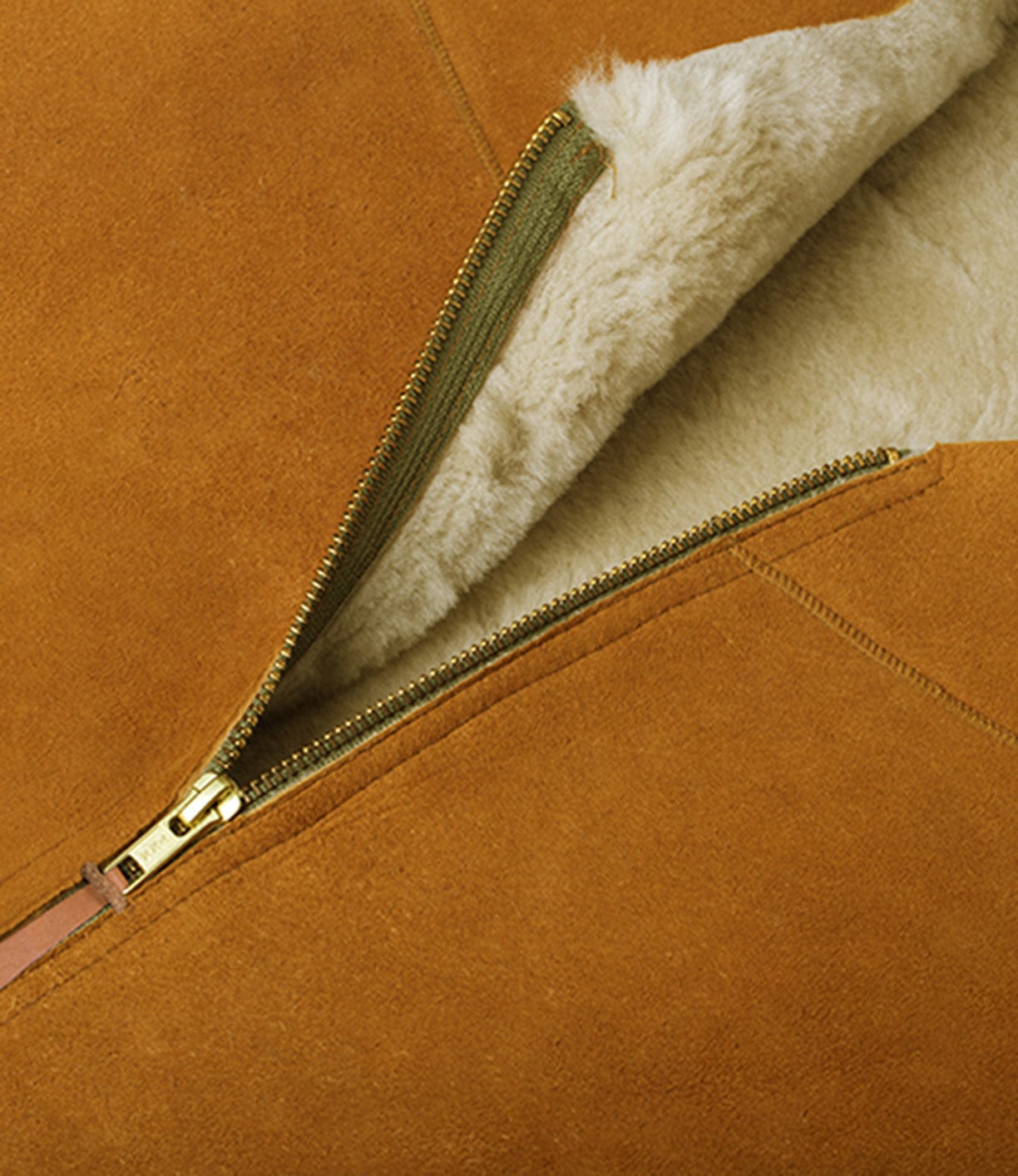 Close-up of a brown suede jacket partially unzipped to reveal white fleece lining. The zipper is gold-colored with a tan fabric strip.