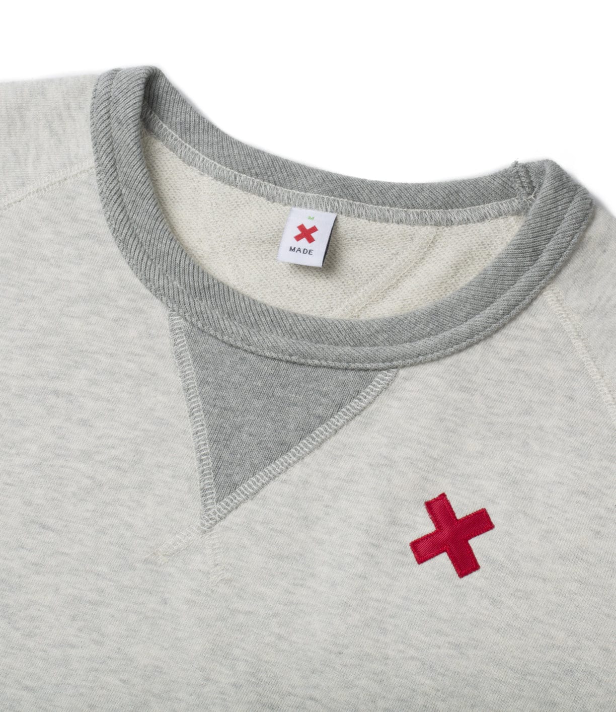 A light gray sweatshirt with a triangular stitching pattern near the neckline and a red X emblem stitched on the left chest.