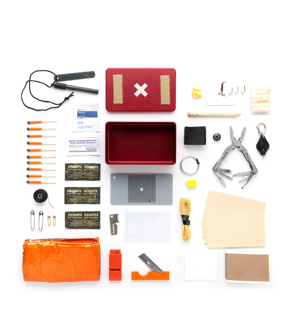 A survival kit spread out, including a first aid box, multi-tool, fire starter, whistle, rope, safety pins, tape, bandages, and various small tools and supplies.