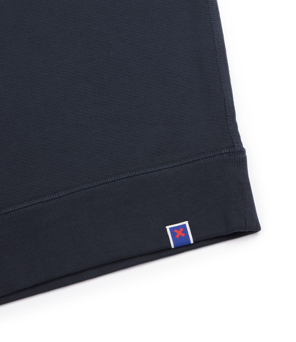 Close-up of the hem of a dark fabric garment featuring a small square tag with a red X on a blue background.