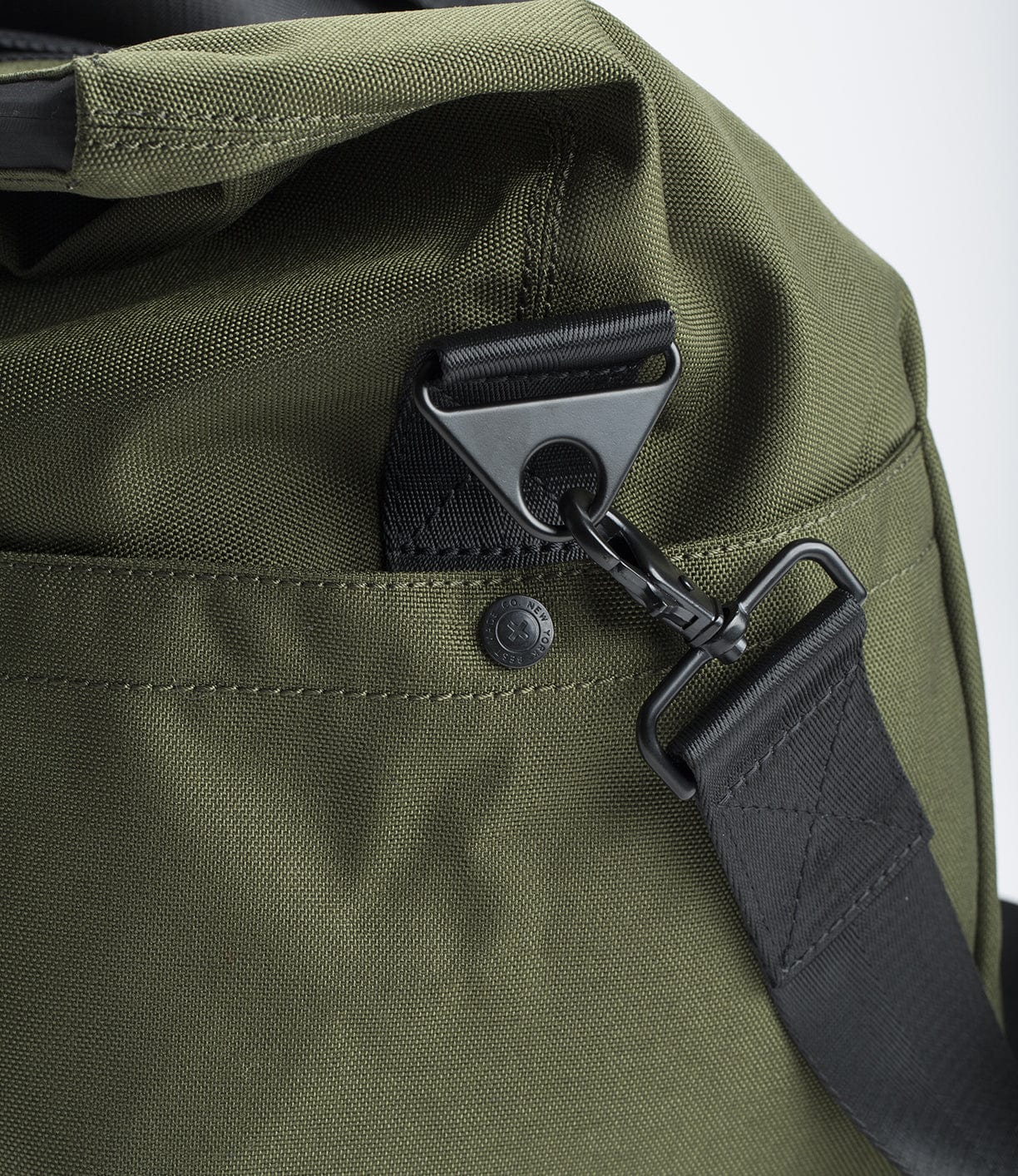 Close-up of a green fabric bag with a black plastic buckle, metal hook attachment, and black adjustable strap.