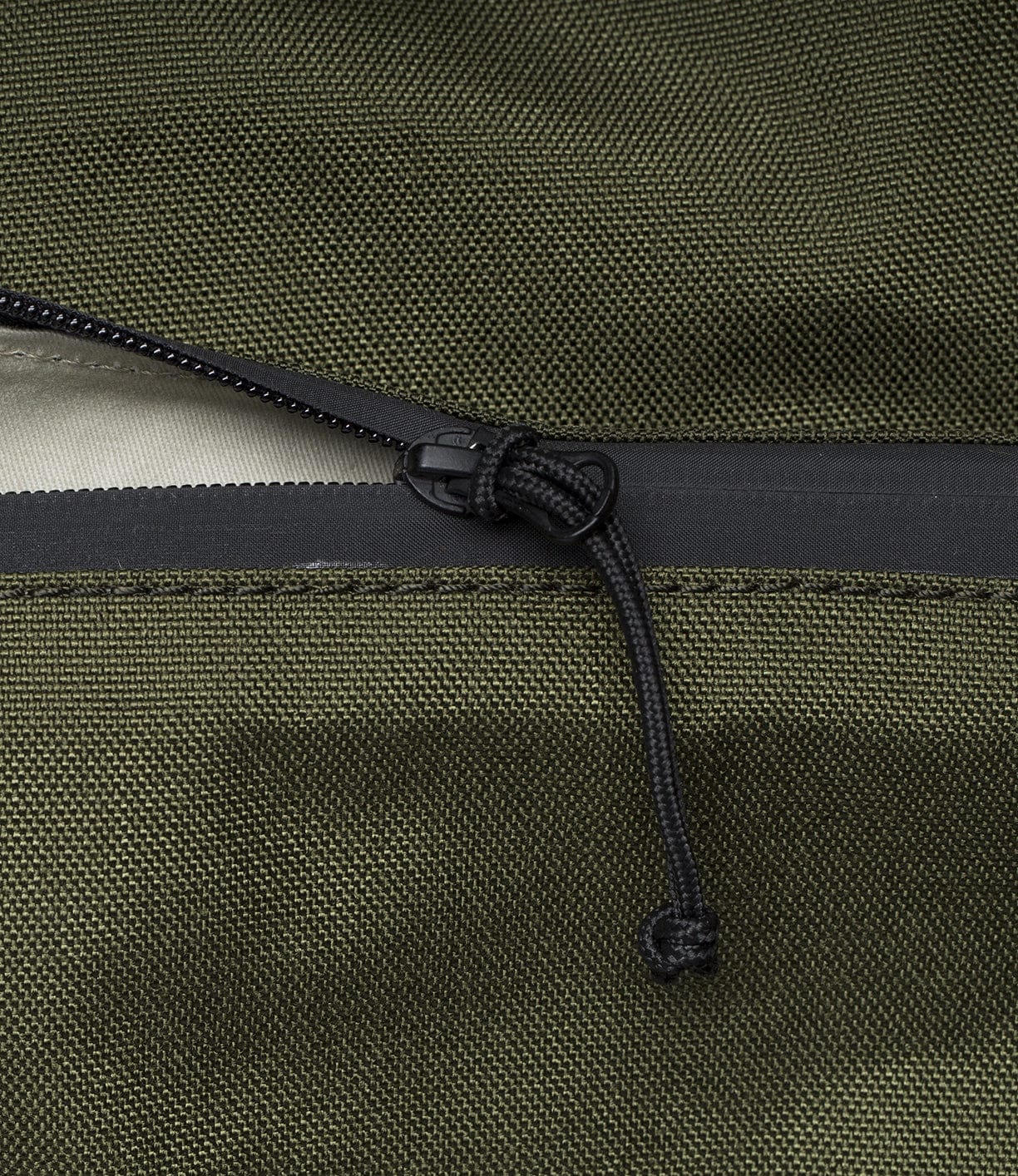 Close-up of a black zipper with a cord pull on a dark green fabric, showcasing the texture and detail of the material.