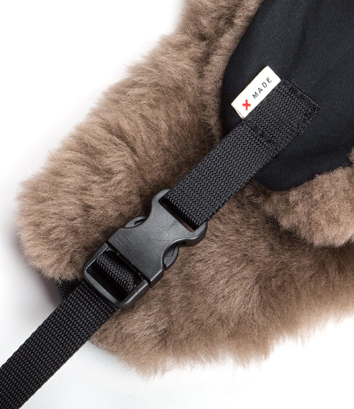 Close-up of a black plastic buckle strap attached to a furry brown fabric and black material, with a small label that reads MADE.