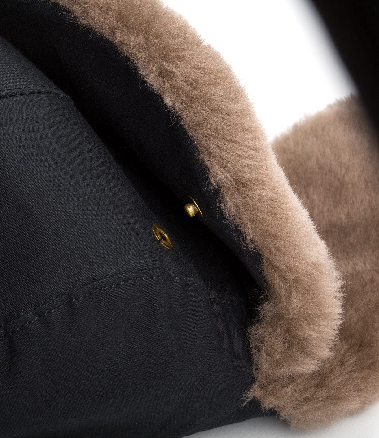 Close-up of the corner of a black fabric item with brown fur lining and visible gold button.