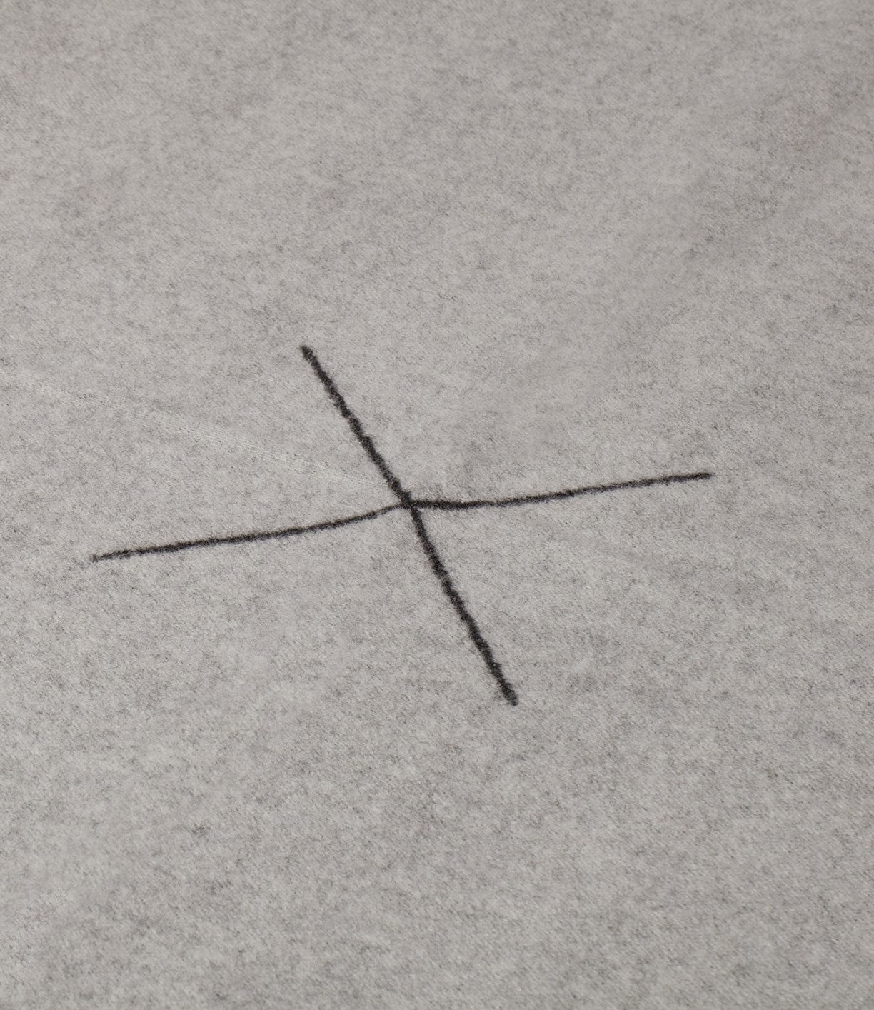 A black cross is drawn on a grey fabric background.