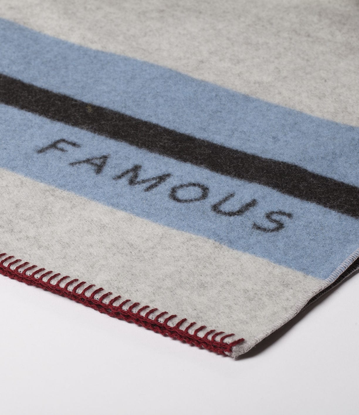 A blanket with blue and black stripes, indicating the word FAMOUS in capital letters. The edge of the blanket has a red stitched border.