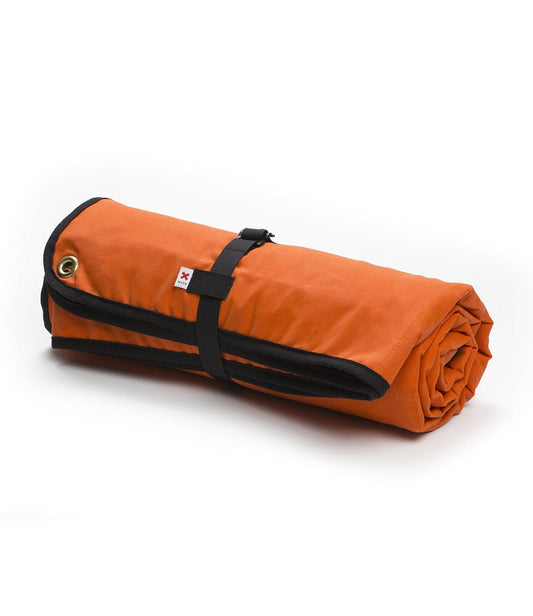 A rolled-up orange sleeping bag with black straps secured around it, featuring a small label.