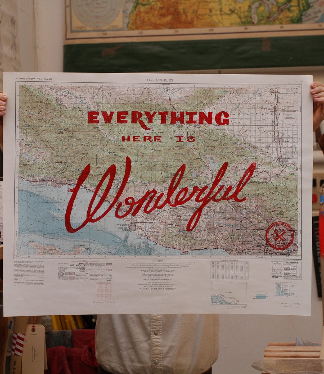 A person holds up a large map of Los Angeles with the words Everything Here is Wonderful written in bold red letters across it.