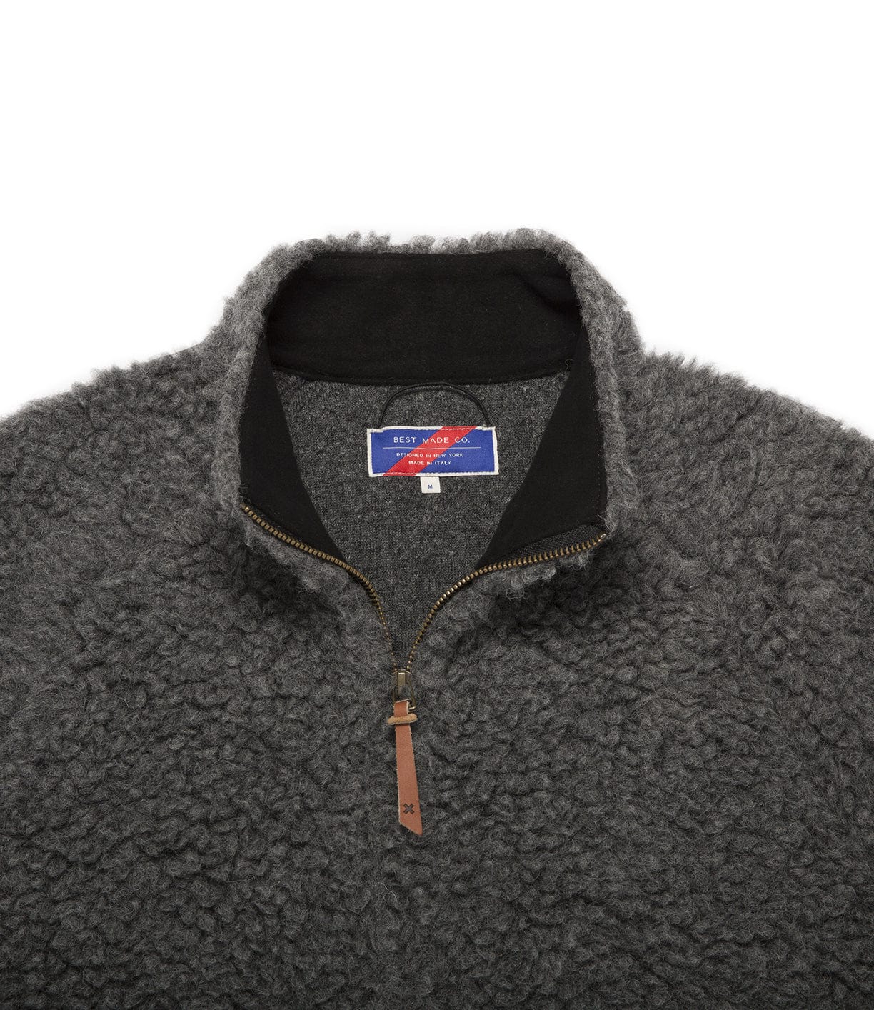 Close-up of a gray, textured fleece with a half-zip front, a tag showing brand information, and a leather pull tab on the zipper.