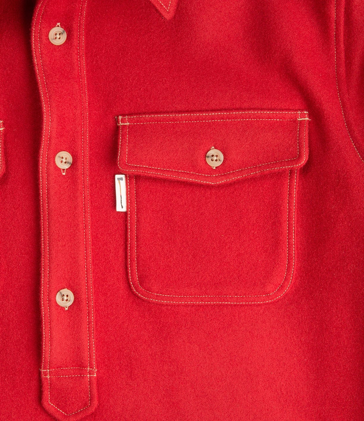 Close-up of a red buttoned shirt featuring a chest pocket with a flap and a small white tag.