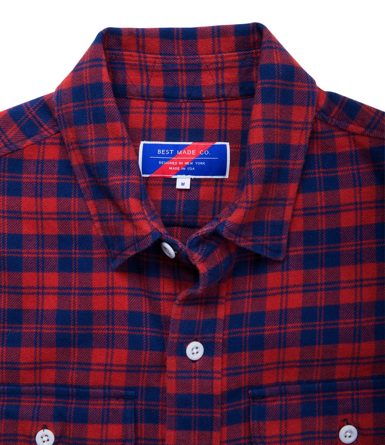 Close-up of a red and blue plaid flannel shirt with a white button-up front. A label at the neck reads Best Made Co. and M.