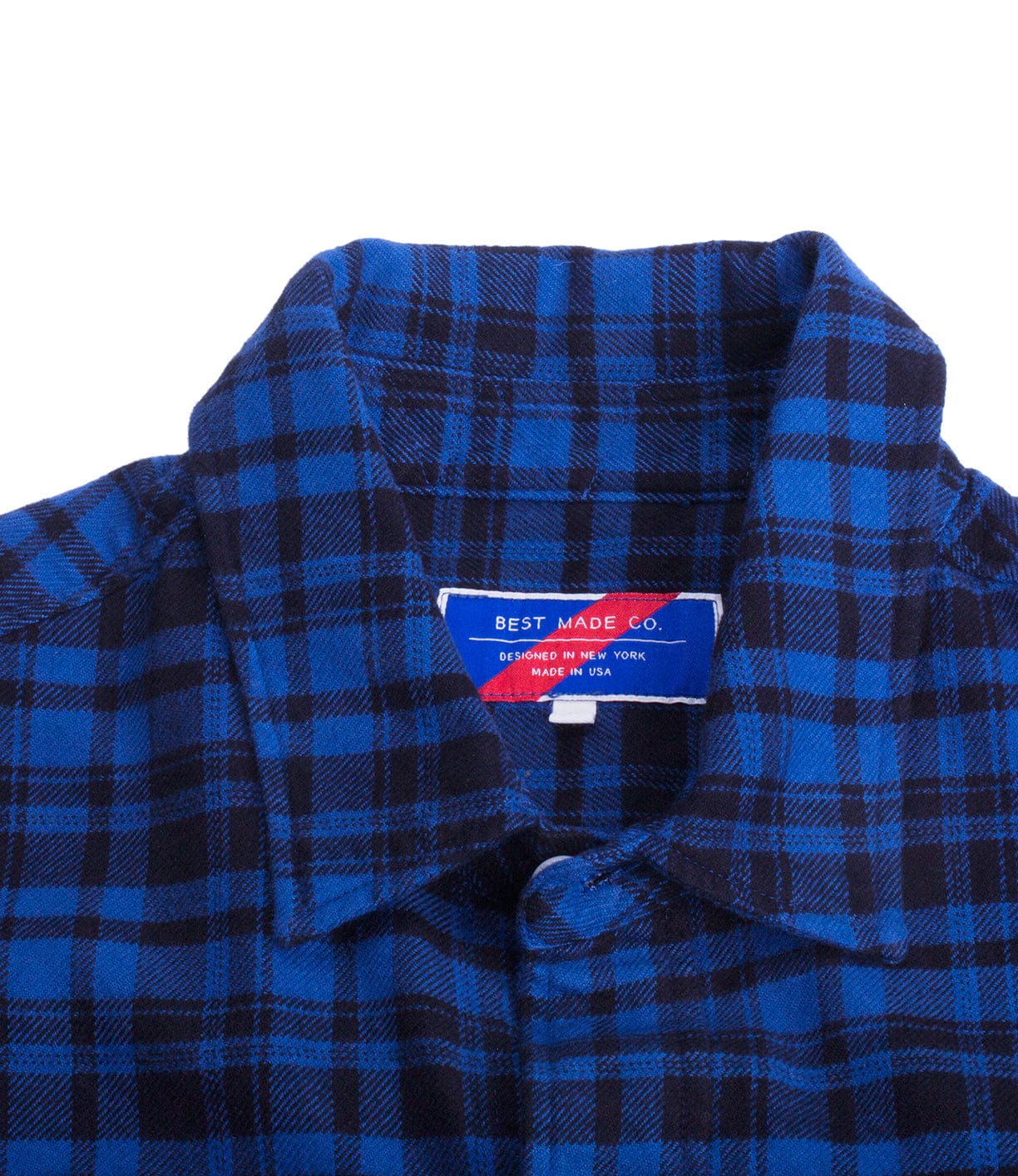 Close-up of a blue and black plaid shirt with a collar. The label inside displays the brand name Best Made Co. and indicates it is designed in New York and made in the USA.